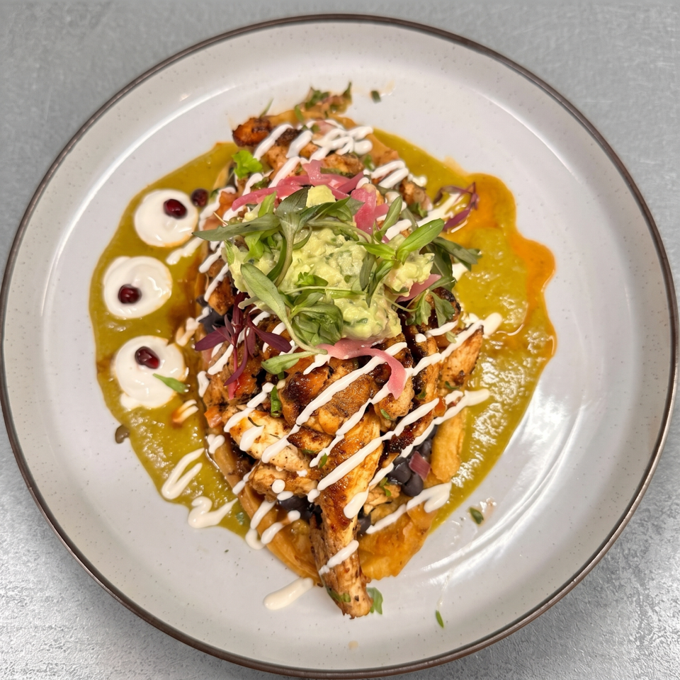 Colorful plated meal with grilled vegetables, avocado, greens, pickled onions, creamy drizzle, beans, and vibrant sauces.