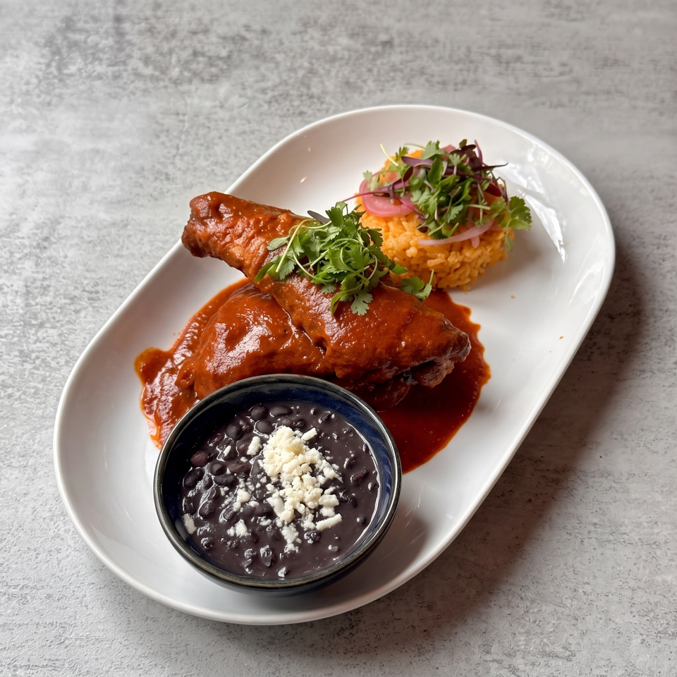 Two enchiladas topped with cilantro, Mexican rice, and refried black beans with crumbled cheese on a white plate.