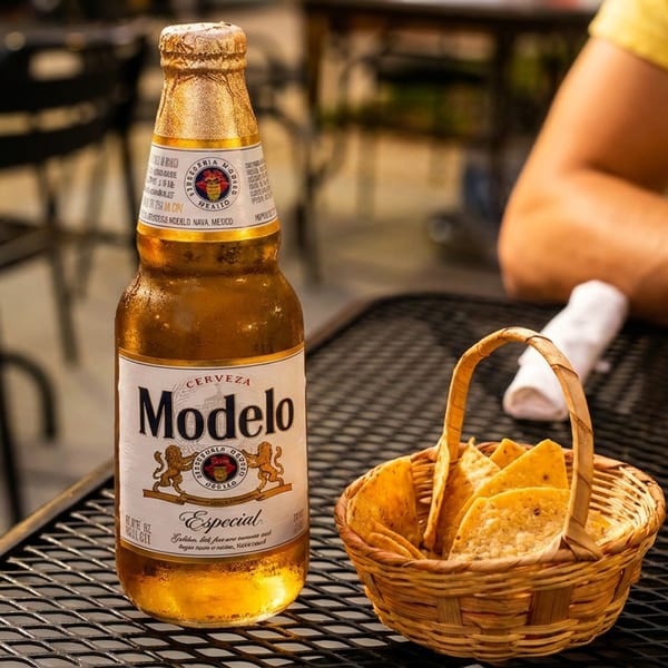 A Modelo Especial beer bottle and a basket of tortilla chips on a patio table.