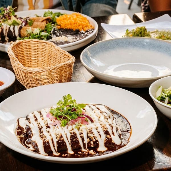 A table laden with Mexican dishes, including enchiladas with mole sauce, rice, beans, and salad.