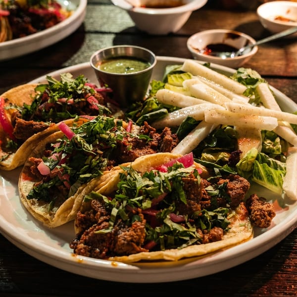 A plate of tacos with meat, cilantro, and pickled onions, served with a side salad.