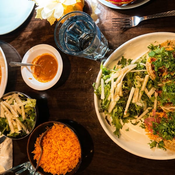 Overhead view of a dark wooden table set with enchiladas, tacos, rice, and a side salad.