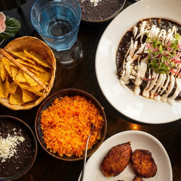 Overhead view of a Mexican meal with mole enchiladas, rice, beans, plantains, salad, and chips.